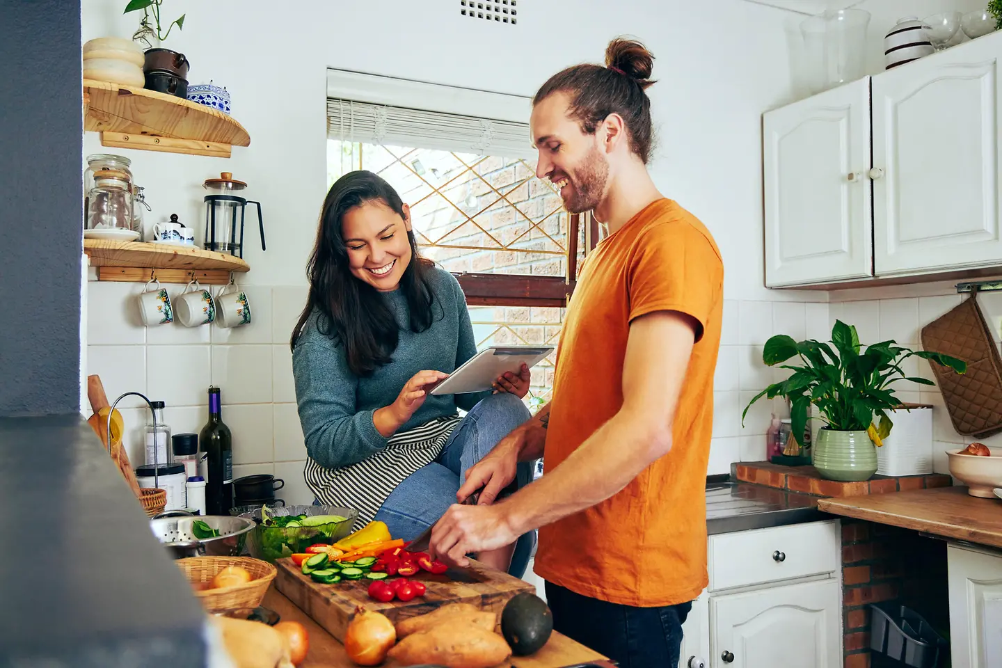 Ein junges Paar kocht gemeinsam mit viel Gemüse, Avocado und Süßkartoffeln