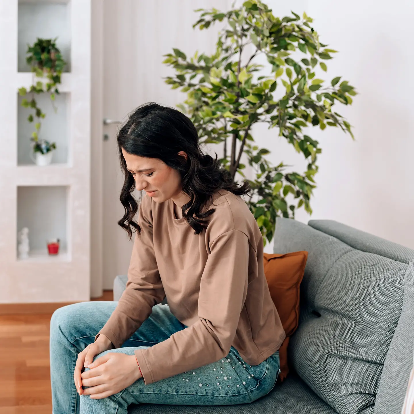 Frau sitzt mit Knieschmerzen auf dem Sofa