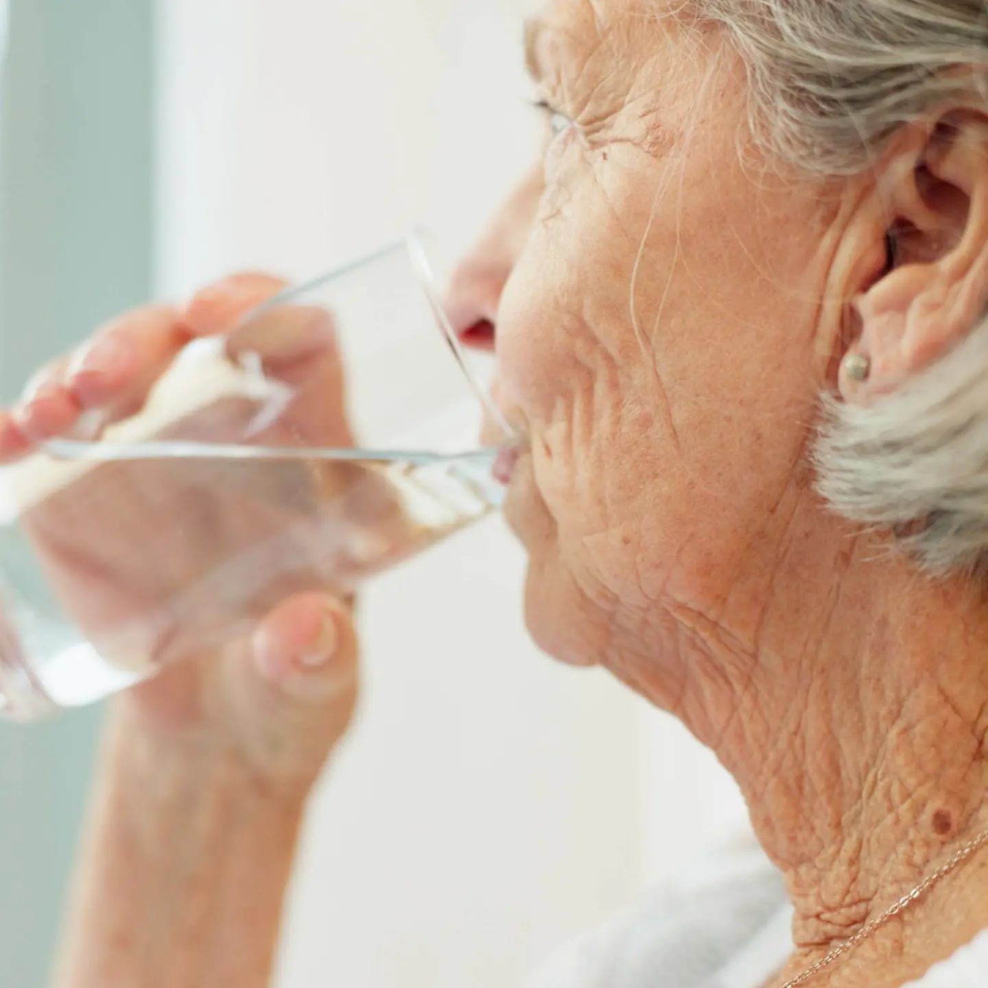 Das Bild zeigt eine ältere Frau im Profil, die sich ein Glas Wasser an den Mund führt. 