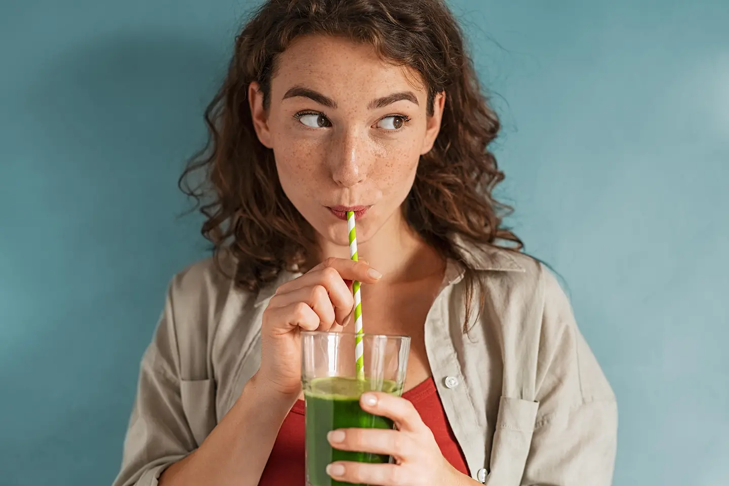 Auf diesem Bild zu sehen ist eine junge Frau, die einen grünen Detox-Smoothie mithilfe eines Papierstrohalms trinkt. 