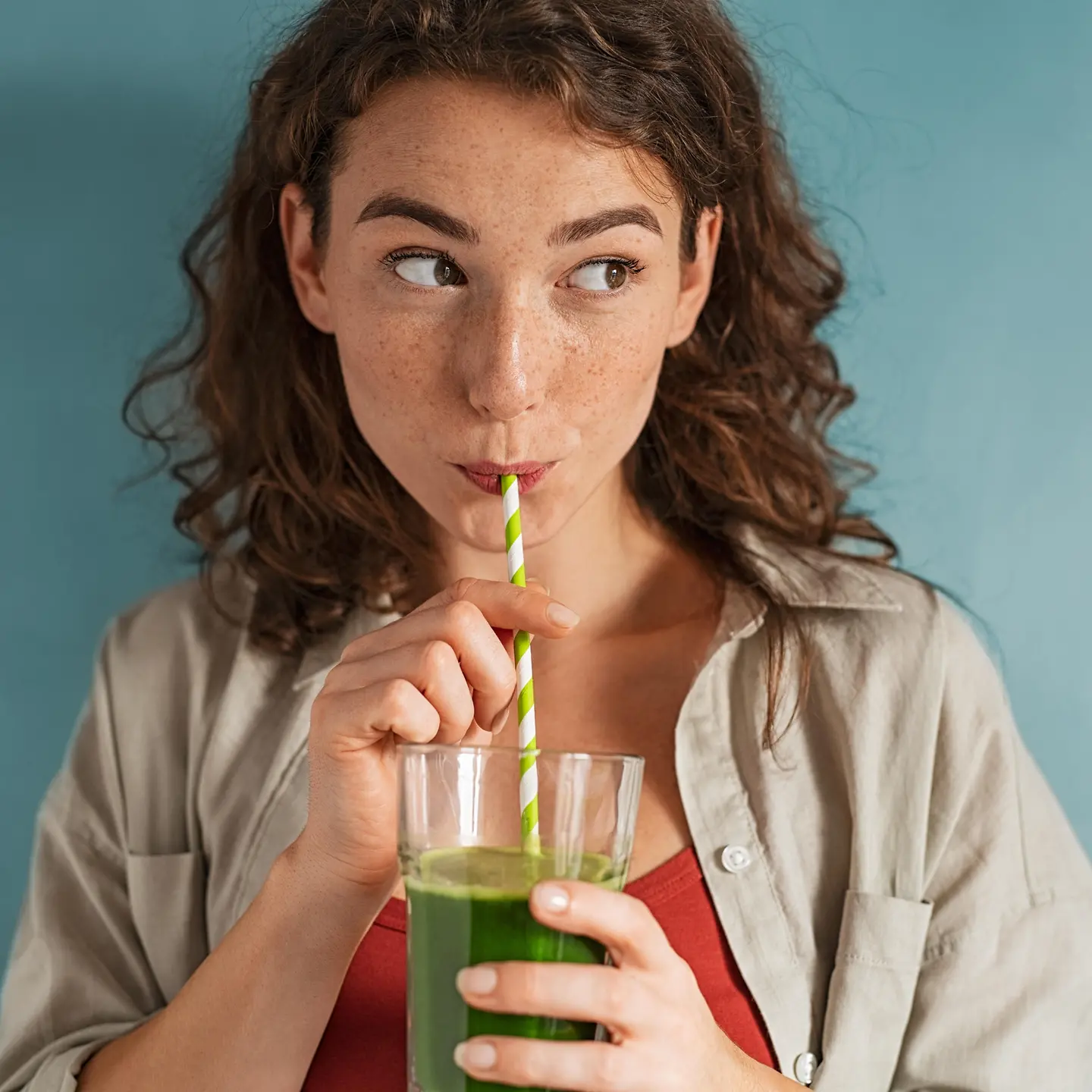Auf diesem Bild zu sehen ist eine junge Frau, die einen grünen Detox-Smoothie mithilfe eines Papierstrohalms trinkt. 