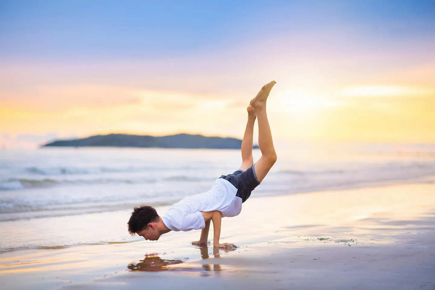 Zu sehen auf dem Bild ist ein junger Mann, der sich allein auf seinen Armen abstützt und mittels des eigenen Gewichts am Strand vor traumhafter Kulisse trainiert. 