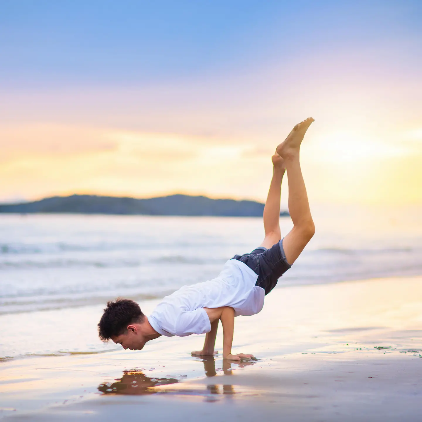 Zu sehen auf dem Bild ist ein junger Mann, der sich allein auf seinen Armen abstützt und mittels des eigenen Gewichts am Strand vor traumhafter Kulisse trainiert. 