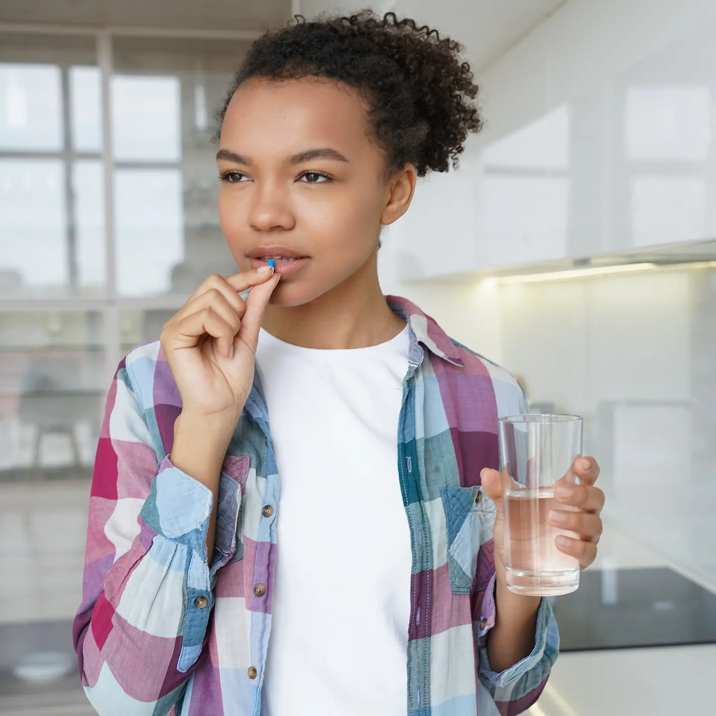 Eine junge Frau in der Küche nimmt Tabletten ein und hält ein Wasserglas