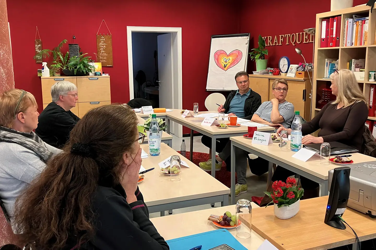 Sechs Menschen sitzen in einem Raum an Tischen und unterhalten sich