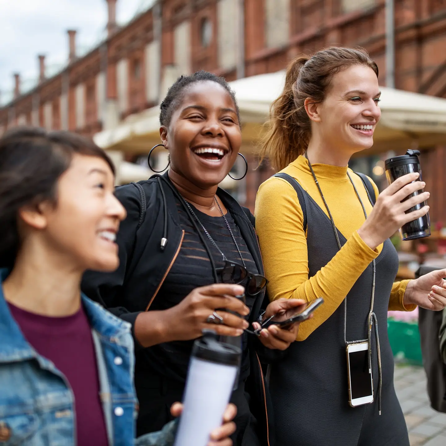 Freundinnen mit Getränken in Händen gehen bei einem Stadturlaub durch eine Einkaufsstraße