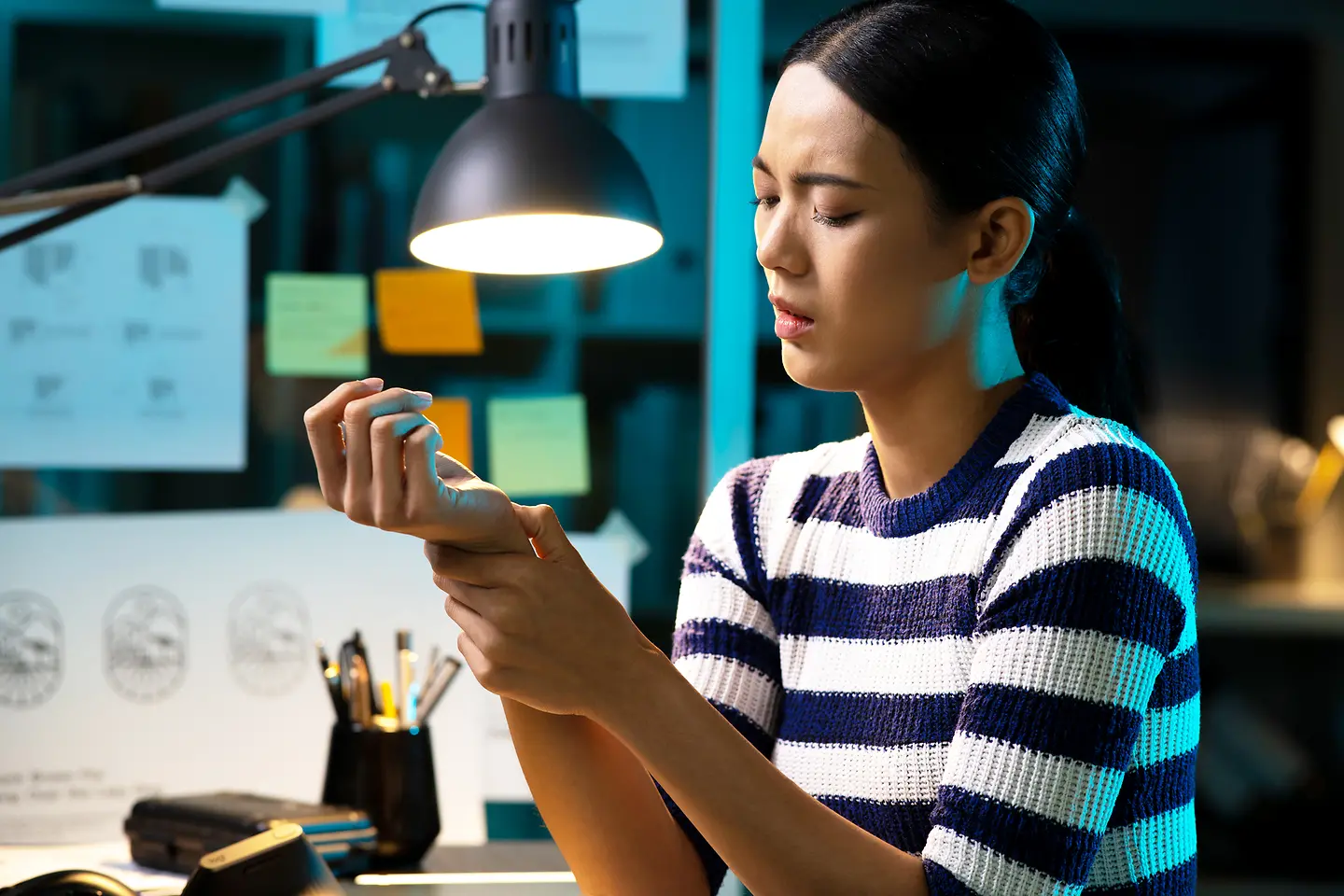 Eine Frau sitzt am Schreibtisch und umfasst schützend ihr Handgelenk.