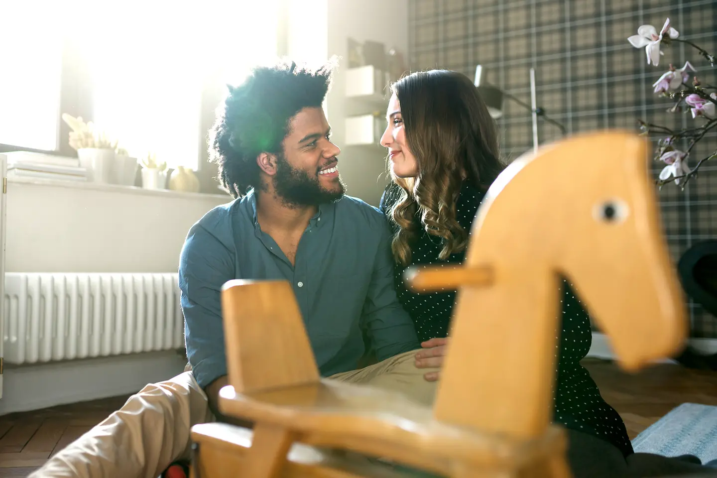 Junges Paar mit Kinderwunsch schaut sich liebevoll an. Im Vordergrund steht ein Schaukelpferd.