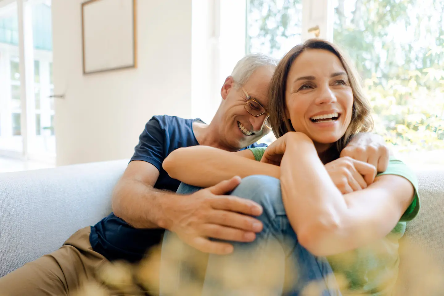 Ein Paar mittleren Alters sitzt zusammen lachend auf dem Sofa.