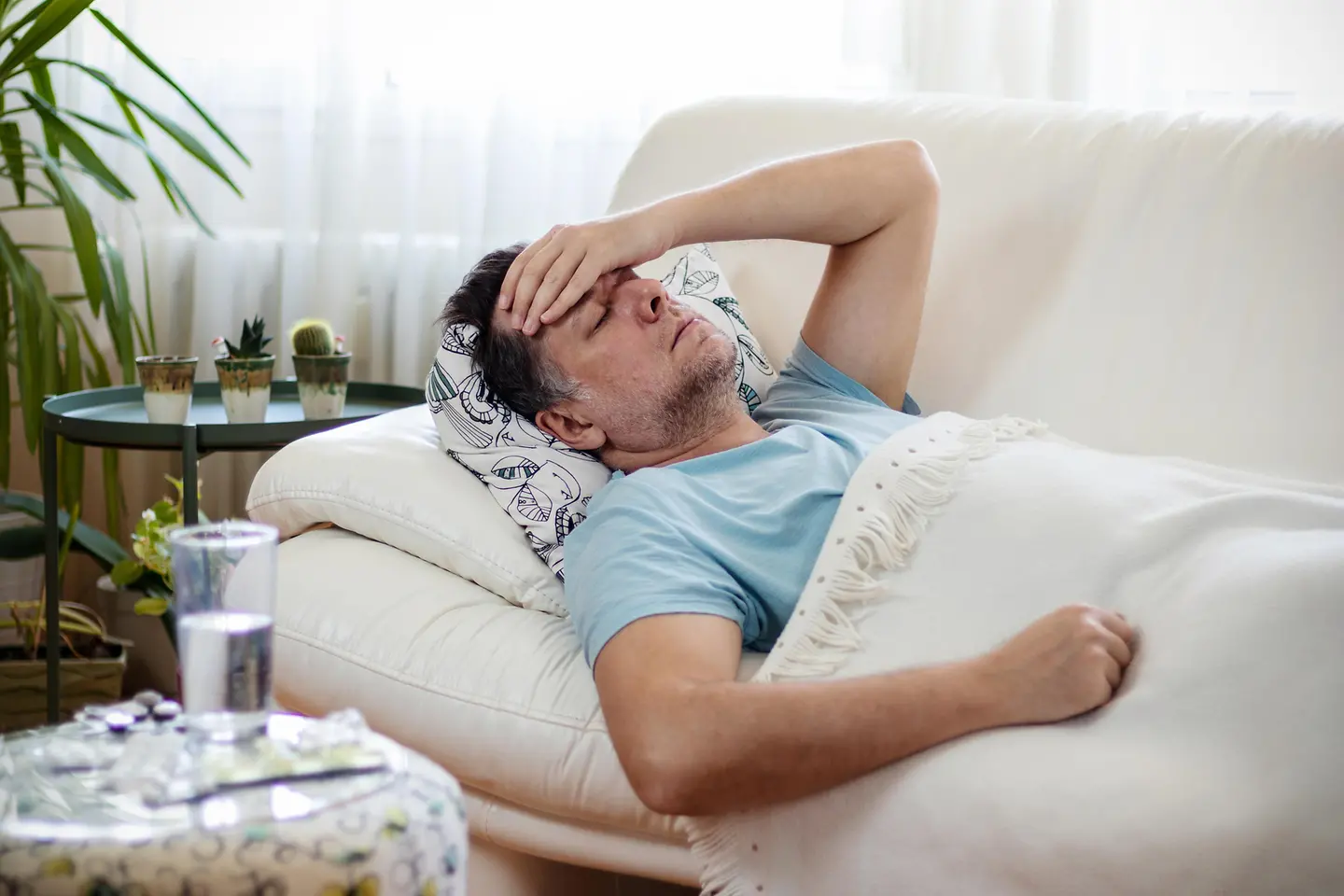Mann liegt mit geschlossenen Augen und sichtlich erschöpft auf dem Sofa und hält sich die Hand an die Stirn.