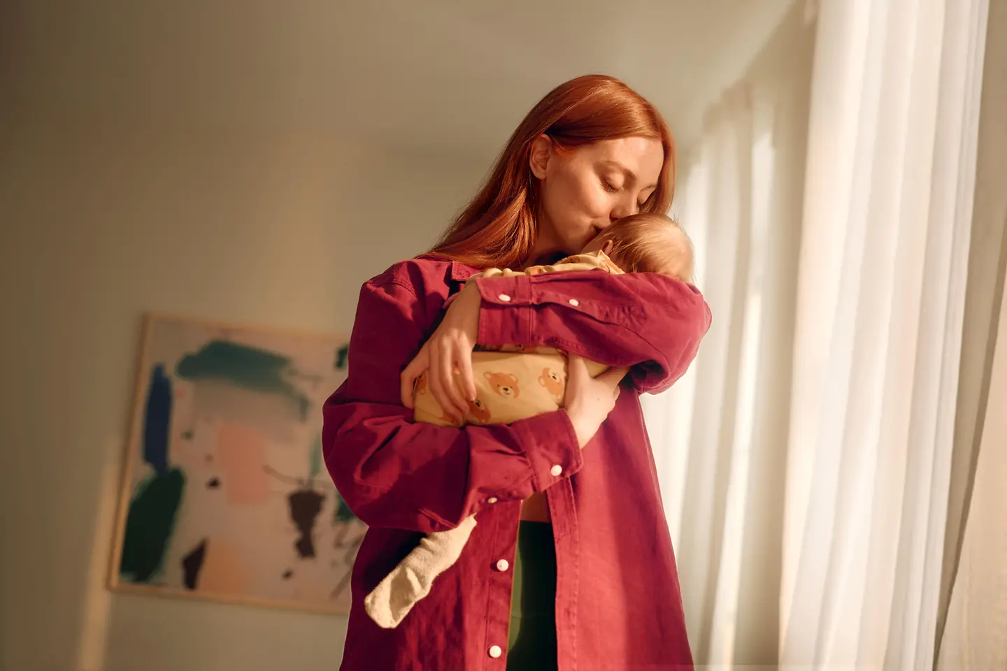 Eine Frau im roten Oberteil hält ihr Baby auf dem Arm. 
