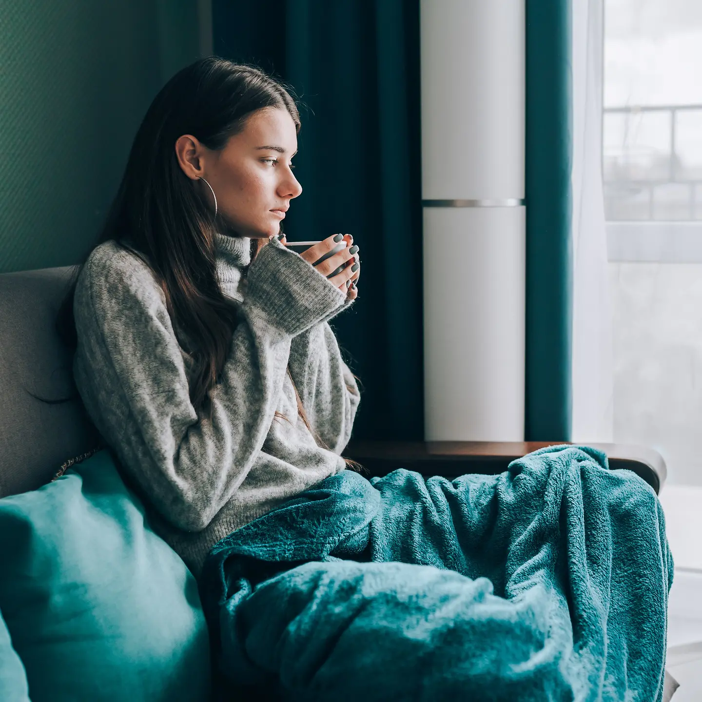 Junge Frau mit Decke und Heißgetränk auf einer Couch