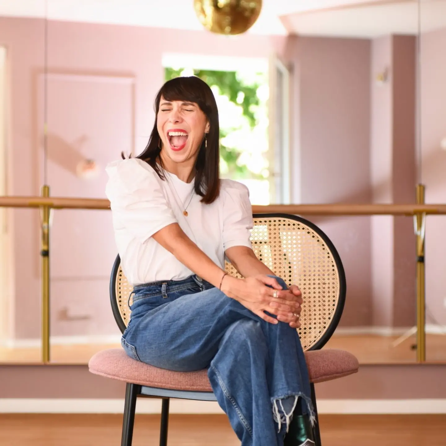 Glücksmama-Gründerin Kristina Basiner sitzt auf einem Stuhl. Sie lacht fröhlich.