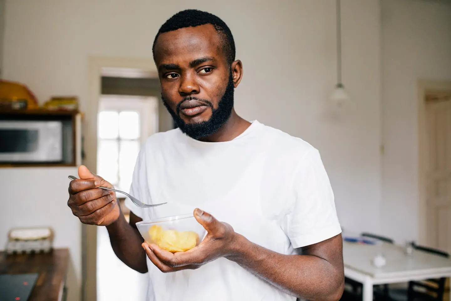 Junger Mann isst mit einer Gabel aus einer kleinen Schüssel