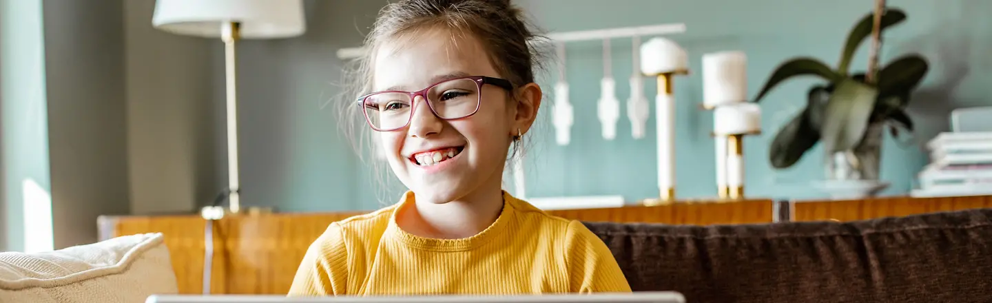 Ein glückliches Mädchen mit einem Laptop auf dem Sofa im Wohnzimmer