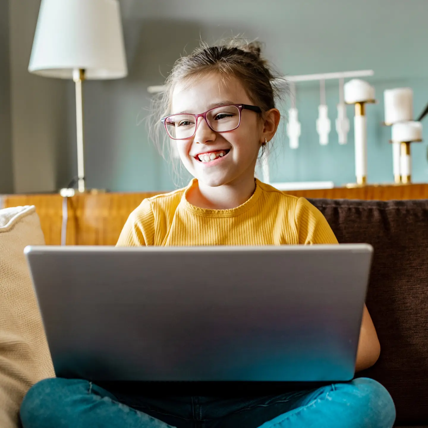 Ein glückliches Mädchen mit einem Laptop auf dem Sofa im Wohnzimmer