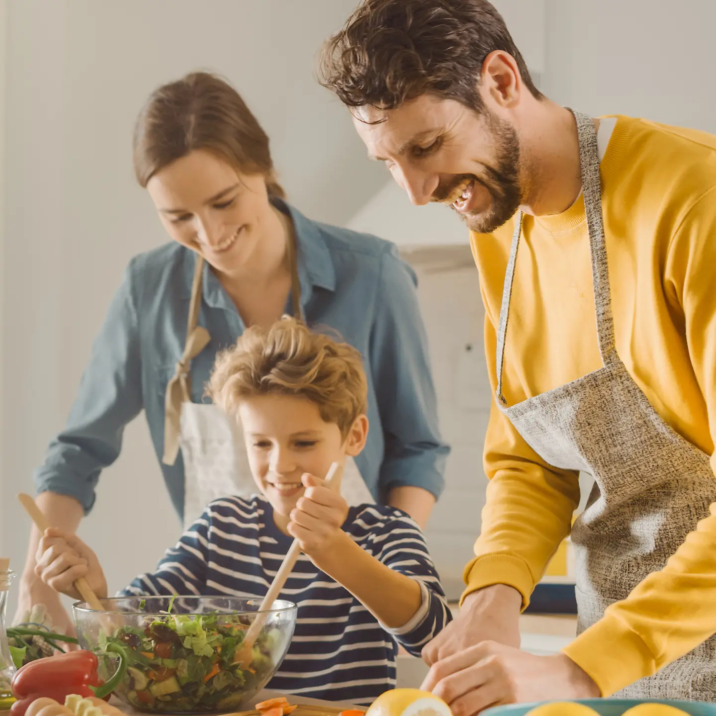 Eine Familie bereitet gemeinsam Essen zu - mit Logos von Barmer, Sarah-Wiener-Stiftung und Ich kann kochen!