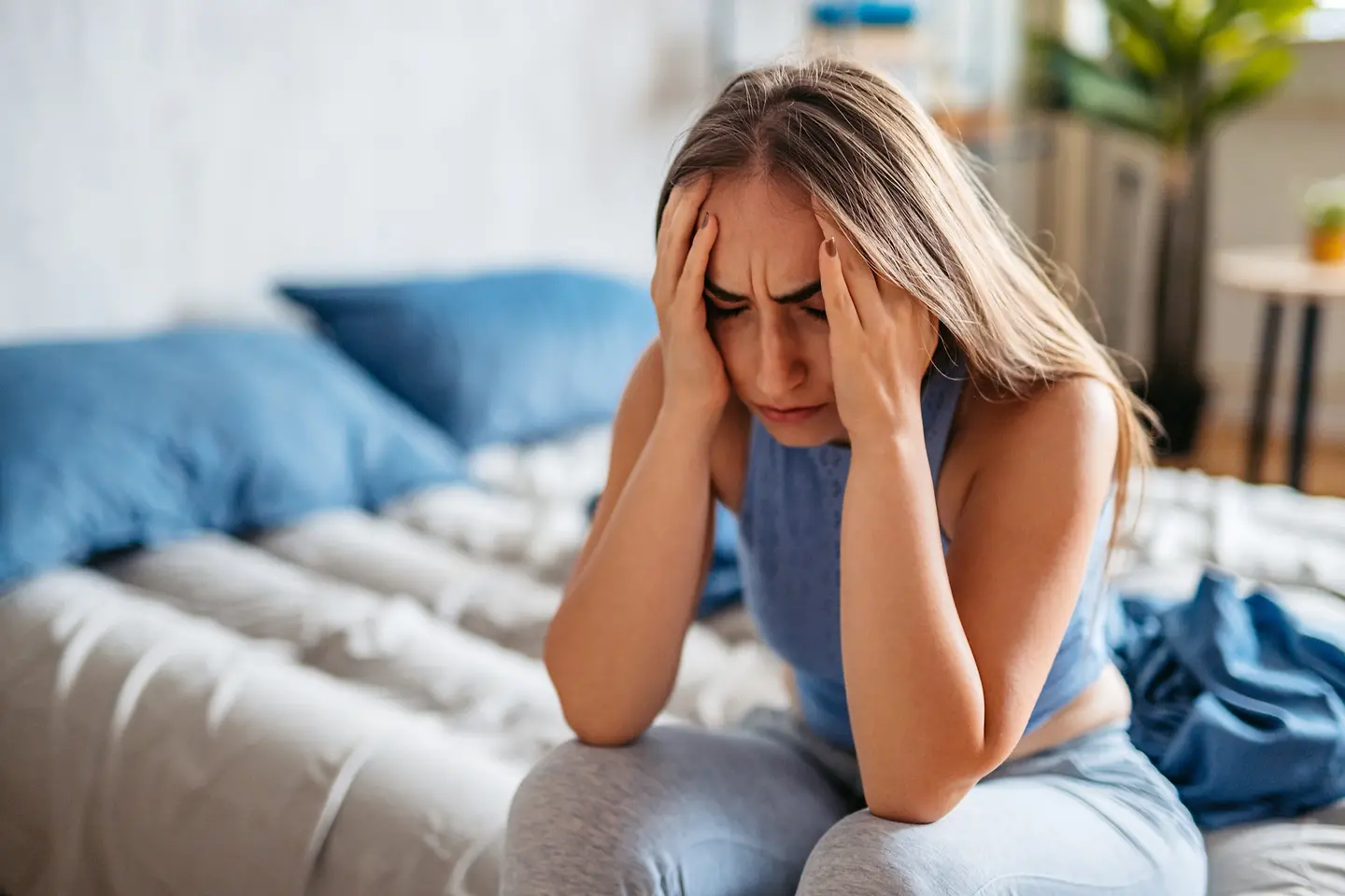 Frau sitzt, sich die Hände an dem Kopf haltend, auf dem Bett
