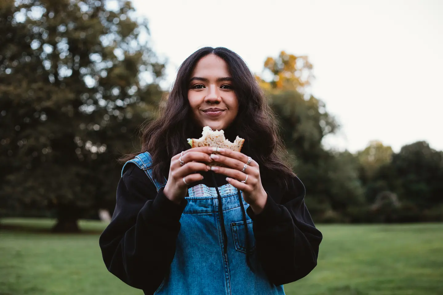 Eine junge Frau isst ein belegtes Brot im Park.
