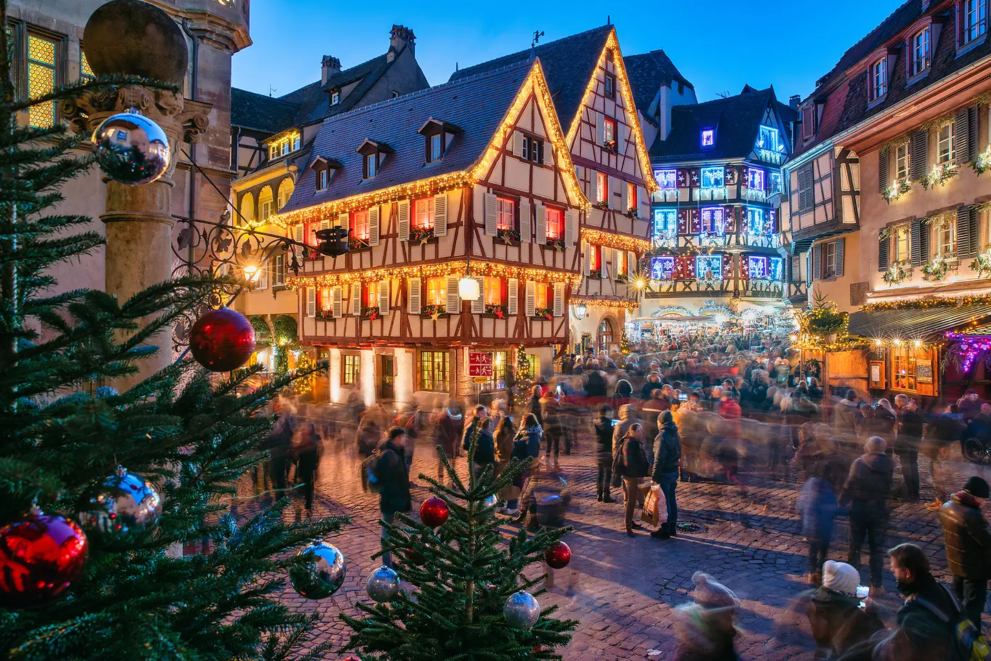 Auf dem Bild zu sehen ist eine weihnachtlich dekorierte Altstadt, wie sie dem weihnachtlichen Klischee entspricht. Es ist bunt, man sieht Tannen, Weihnachtsbaumkugeln.