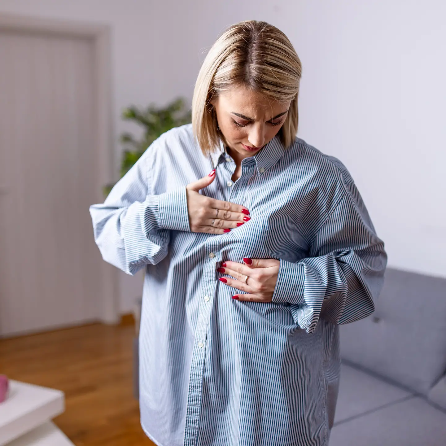 Eine junge Frau steht in ihrem Wohnzimmer und tastet ihre Brust ab