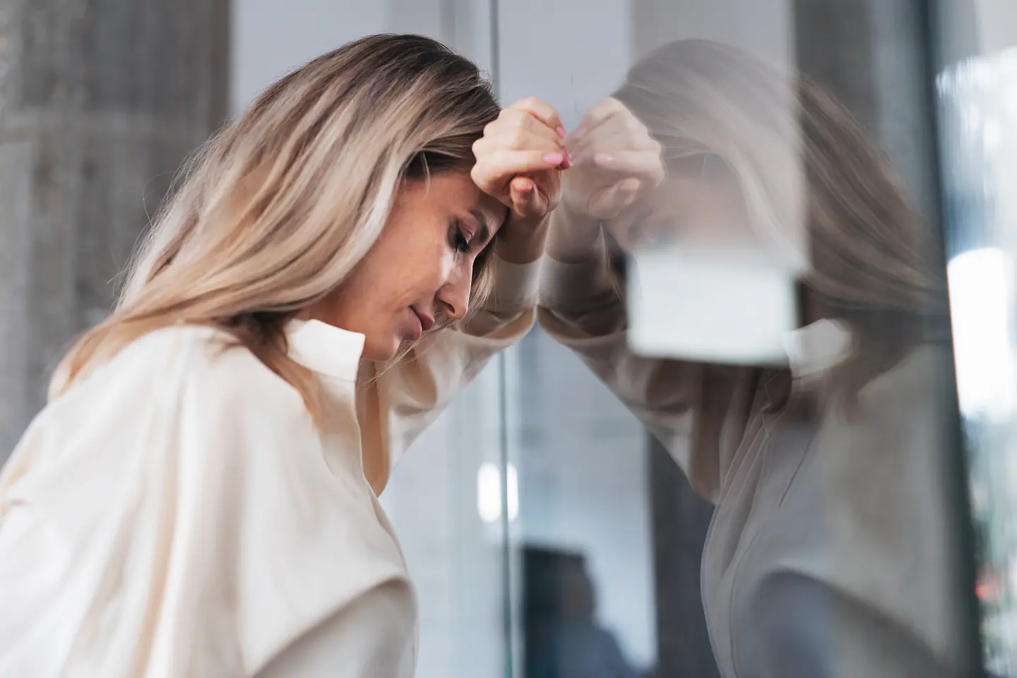 Berufstätige Frau mit Kopfschmerzen lehnt gegen eine Glasscheibe im Büro