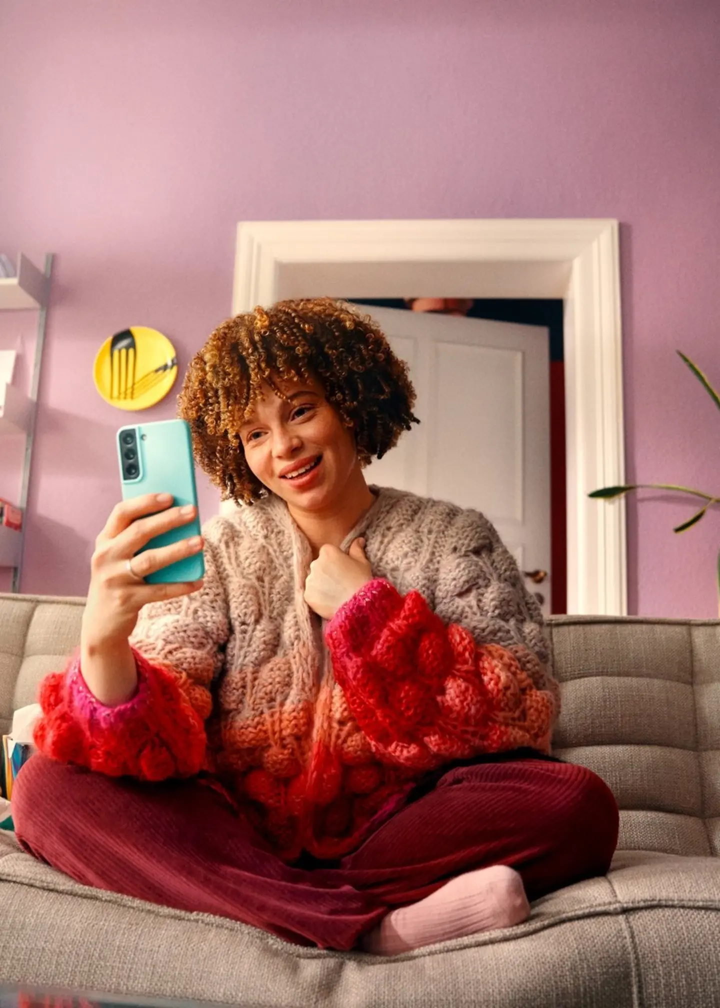 Eine junge Frau mit Afro-Frisur sitzt auf dem Sofa und schaut in ihr Smartphone