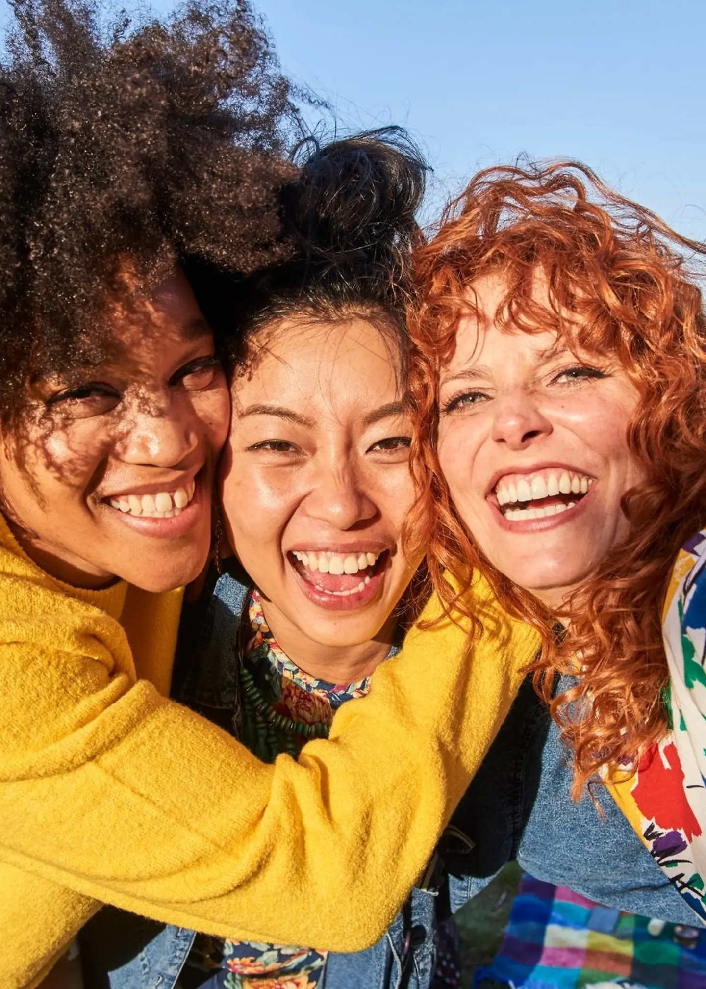 drei junge Frauen lächeln in die Kamera, ihre Gesichter nah beieinander