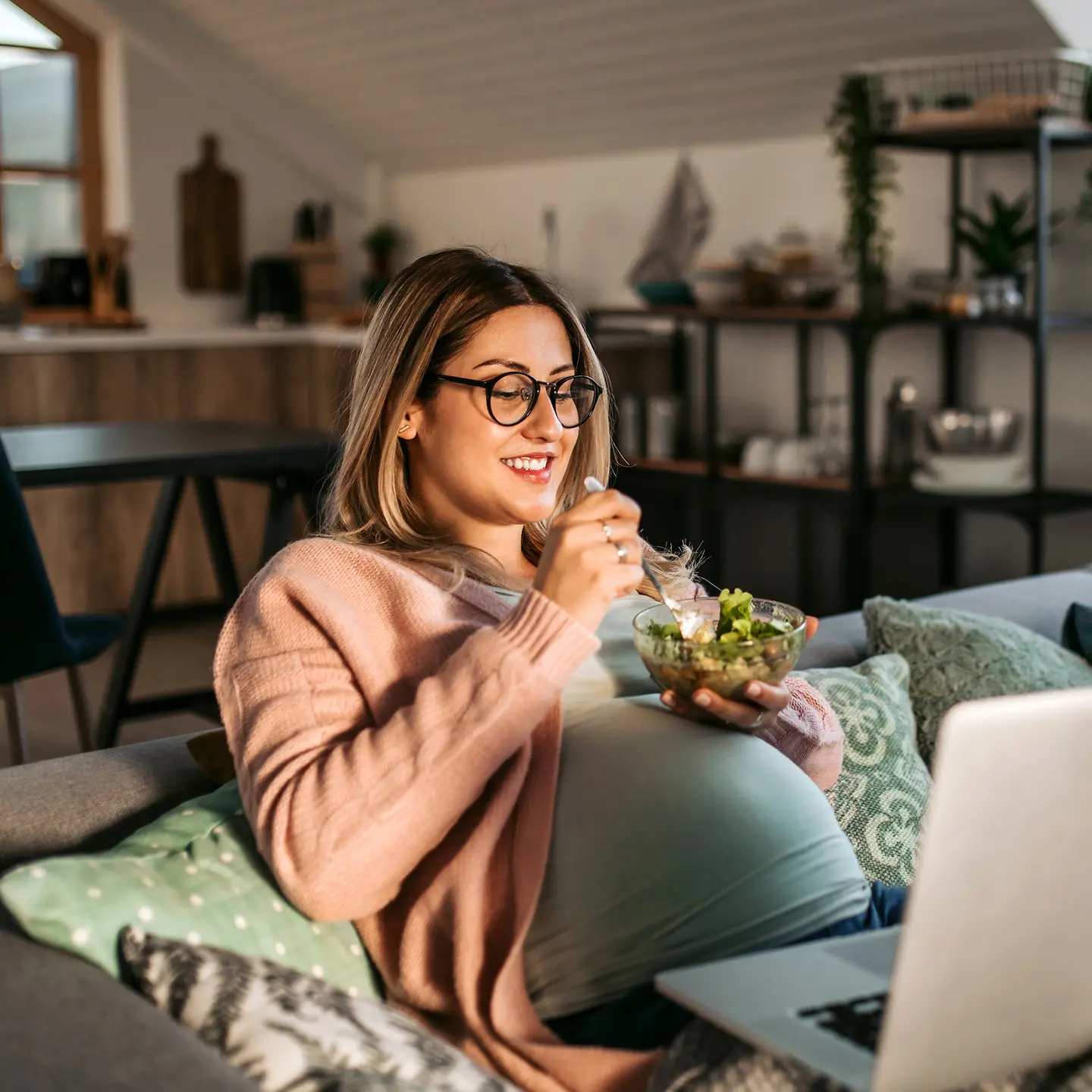 Eine junge schwangere Frau sitzt auf einer Couch und isst aus einer Schüssel