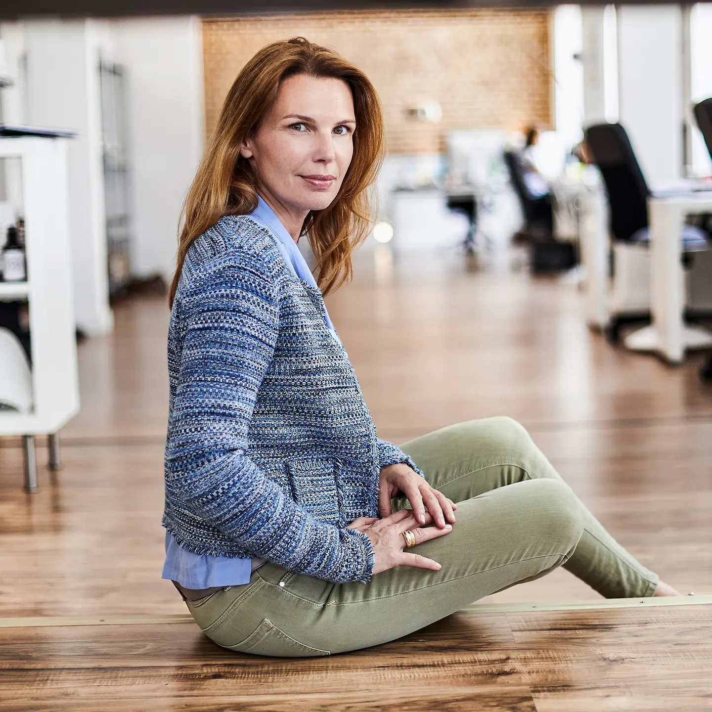 Eine Frau sitzt auf einer Holzstufe in einem Großraumbüro und schaut in die Kamera