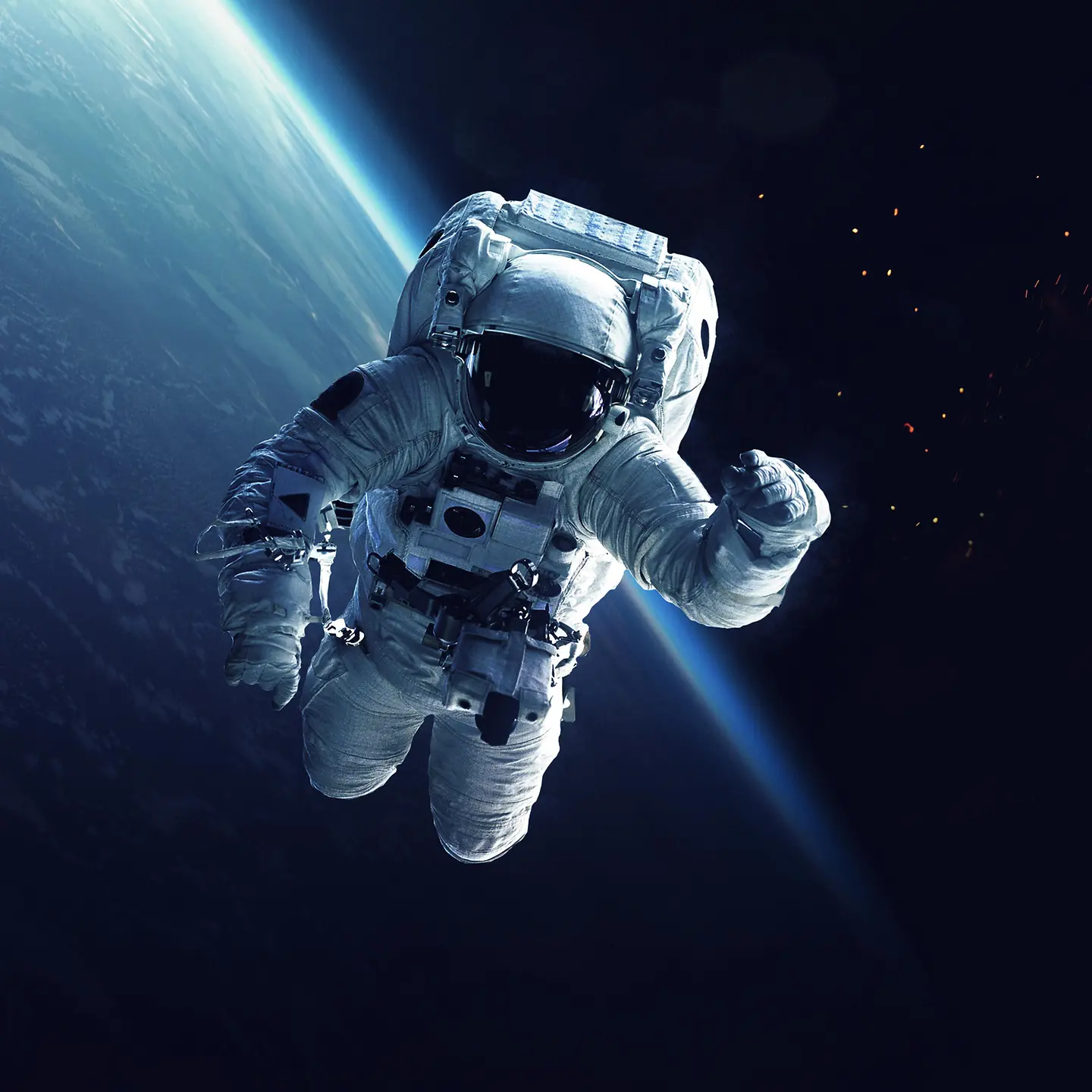 Auf diesem Bild zu sehen ist ein Astronaut im All. Er schwebt. Sein linker Arm ist erhoben. Hinter ihm ist das dunkle Weltall und ein Teil des blauen Planeten Erde zu erkennen. 
