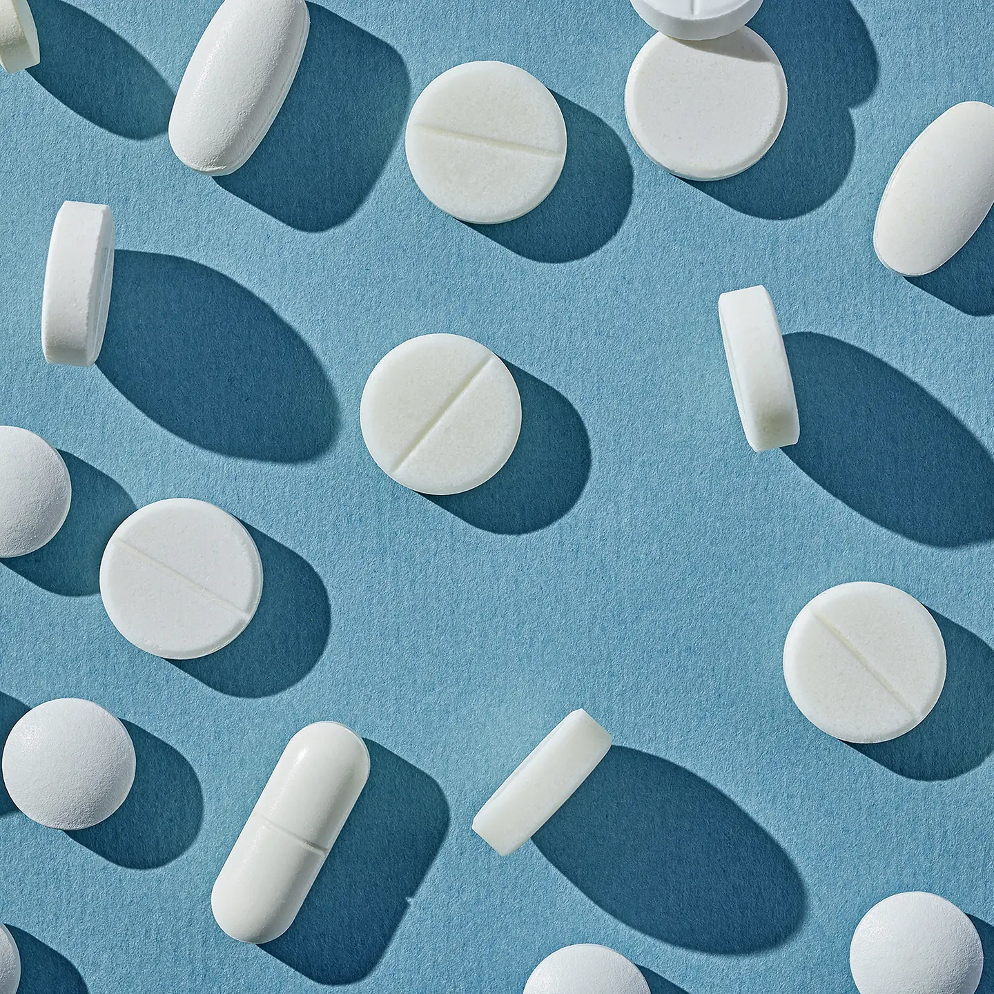 Auf dieser Illustration ist eine Vielzahl von weißen Tabletten in verschiedenen Formen auf blauem Untergrund zu sehen.