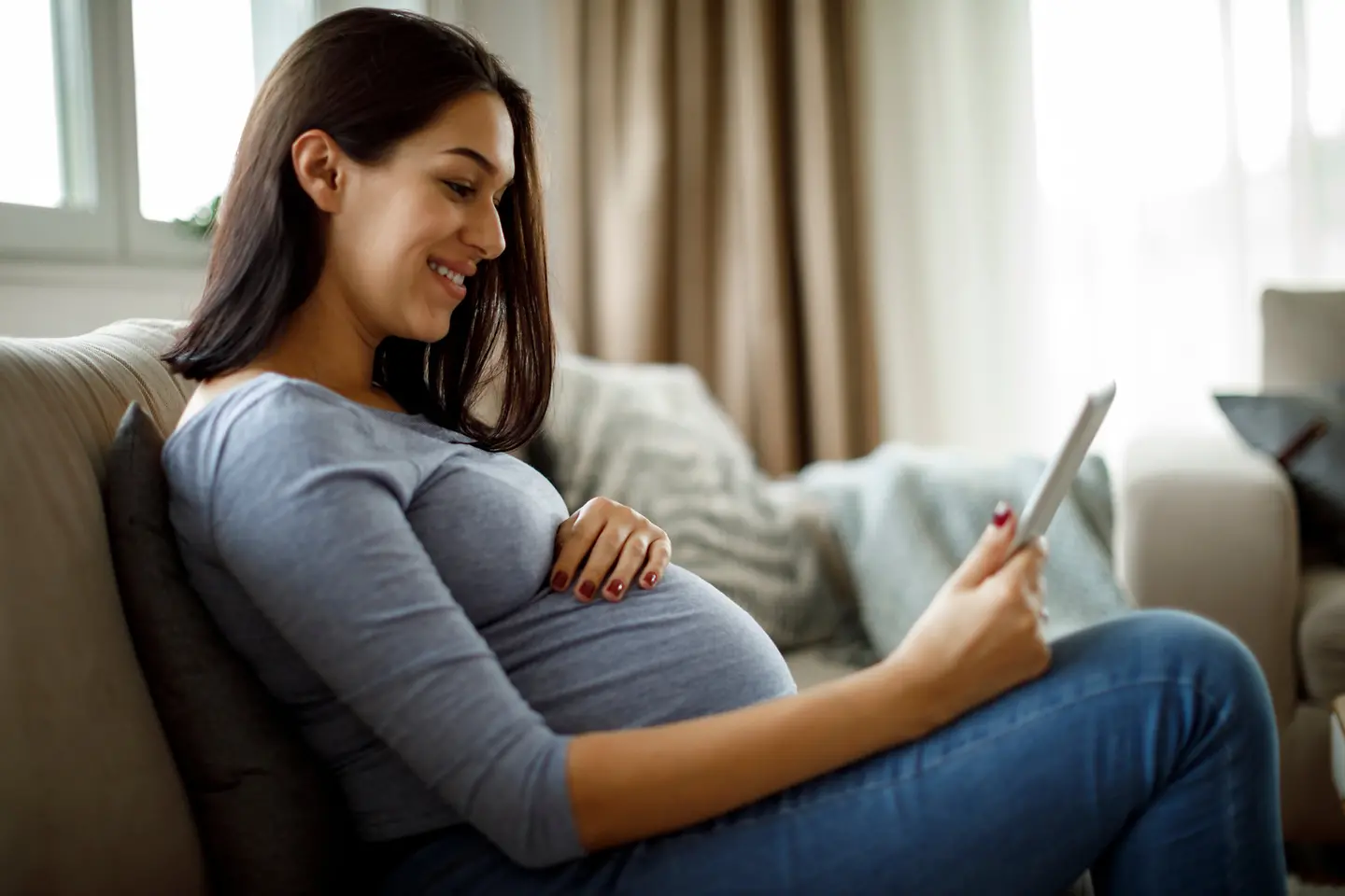Eine Schwangere sitzt auf der Couch mit Smartphone in der Hand