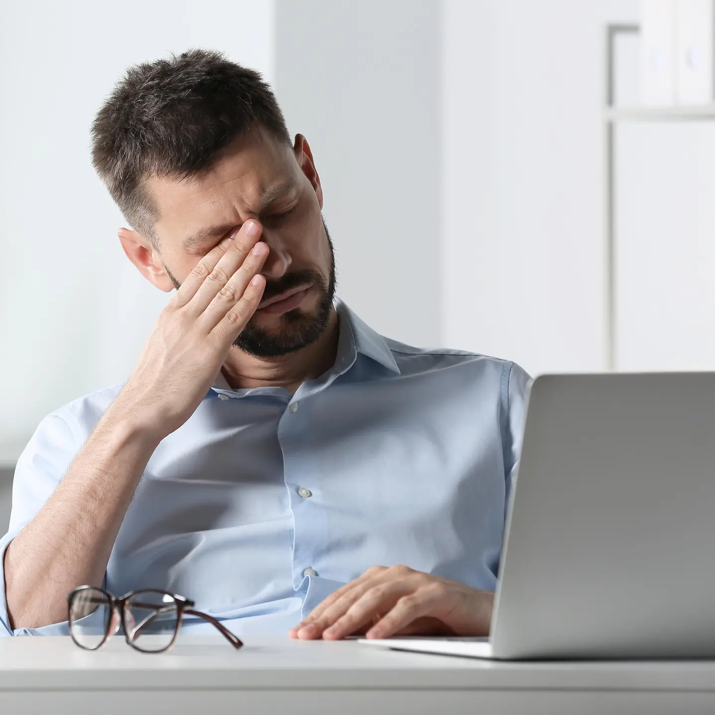 Mann sitzt am Laptop und reibt sich ein Auge