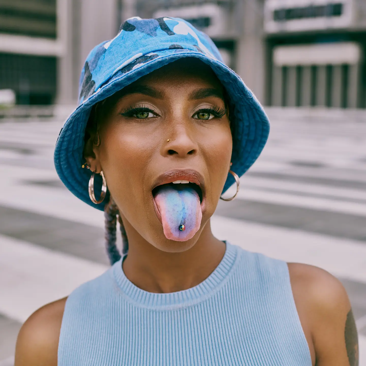 Eine junge Frau mit Hut streckt ihre blau gefärbte Zunge raus