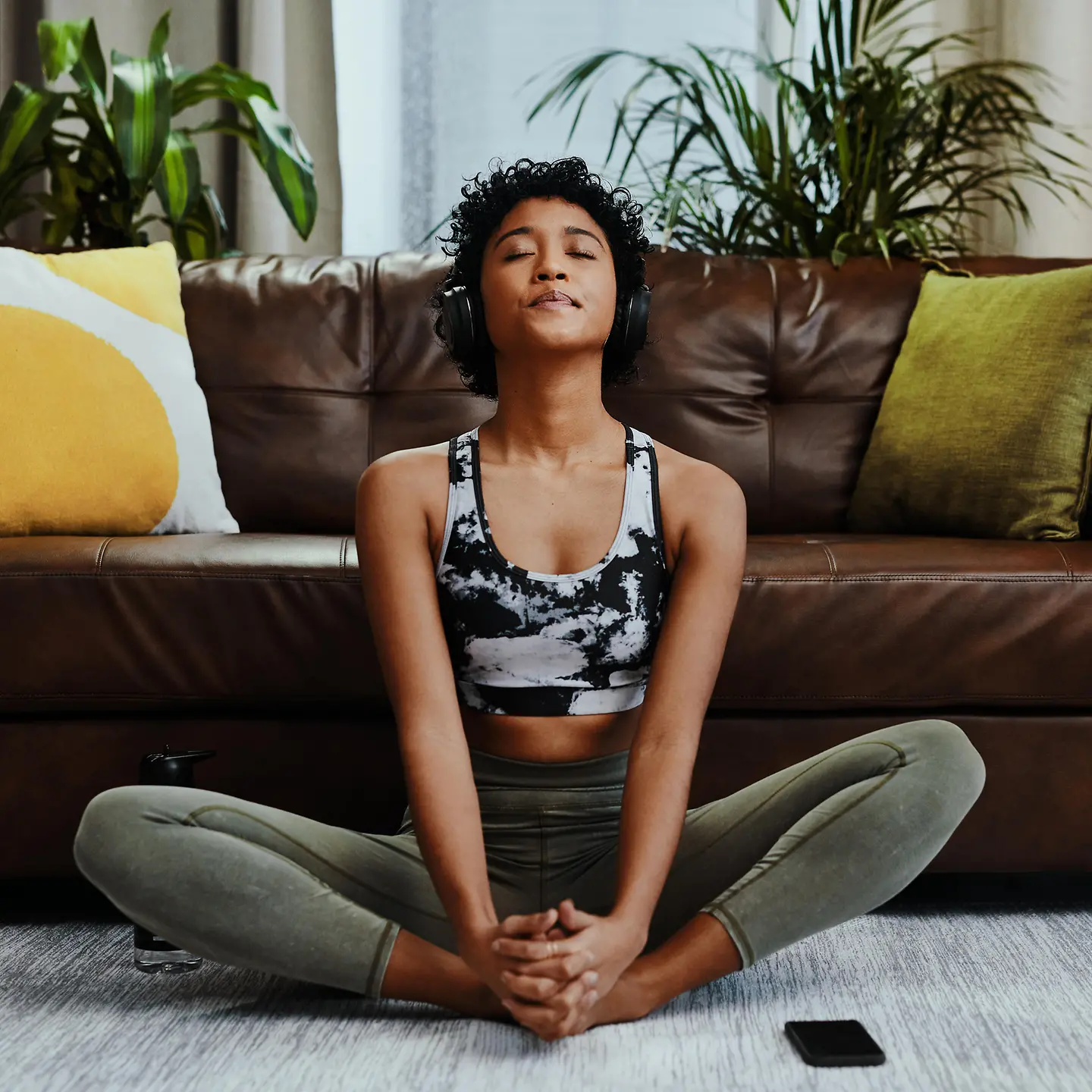 Junge Frau meditiert mit Kopfhörern vor dem Sofa