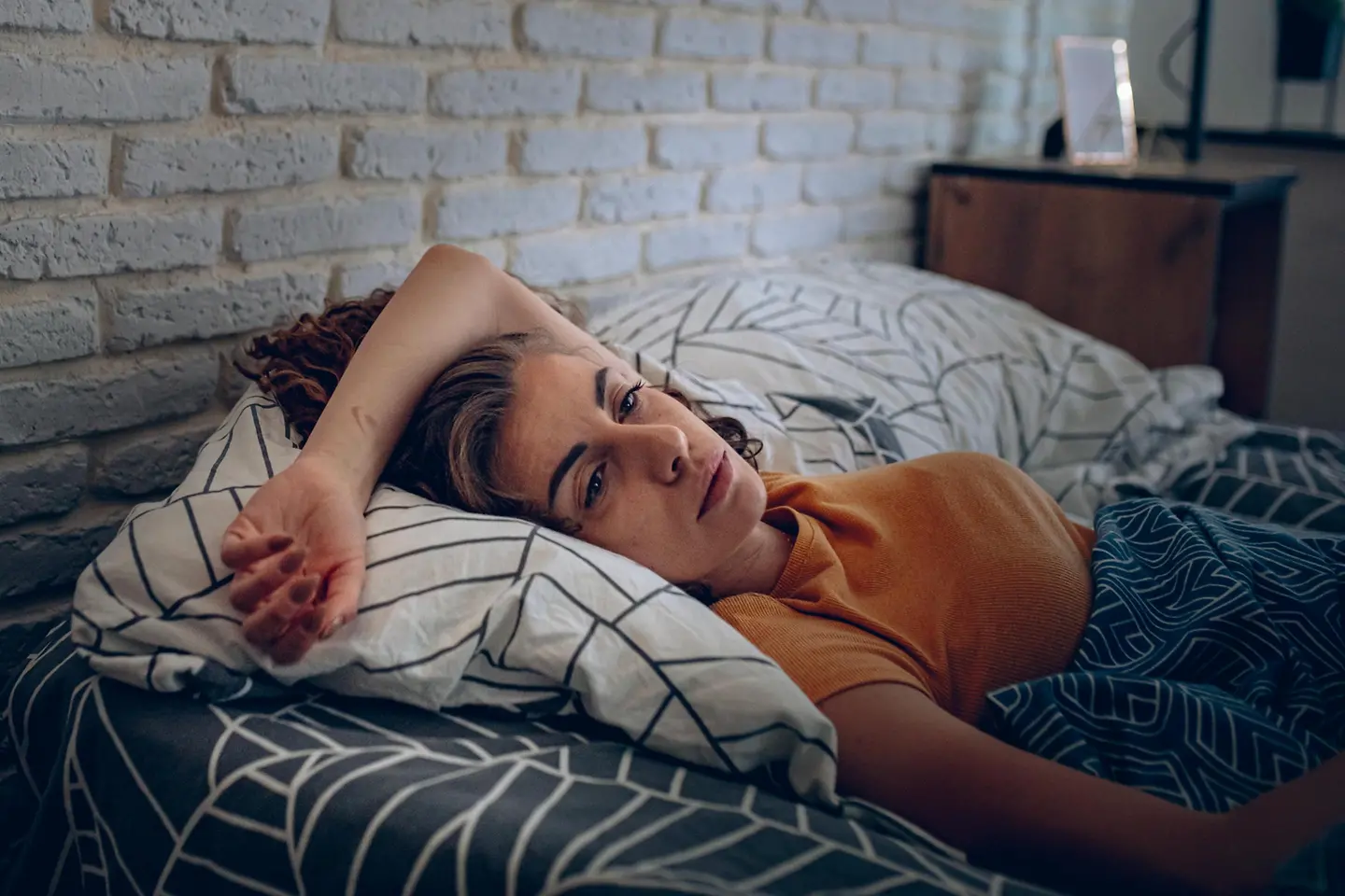 Junge Frau liegt erschöpft mit offenen Augen im Bett