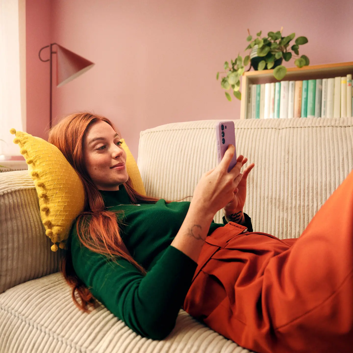 Eine Frau sitzt auf einem Sofa und hält ein Smartphone in der Hand, auf dem sie die Barmer-App nutzt.
