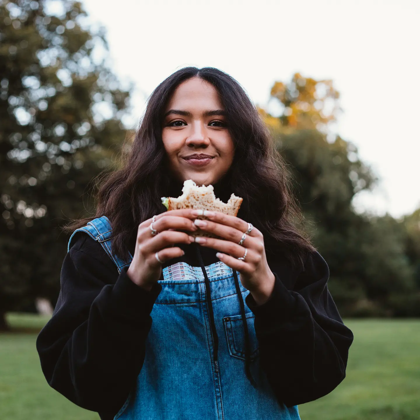 Eine junge Frau isst ein belegtes Brot im Park.
