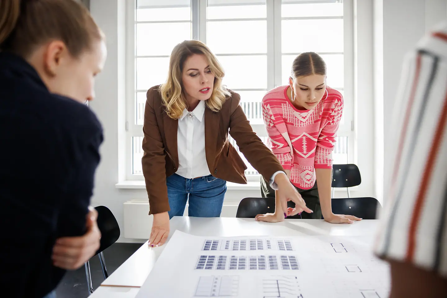 Eine Geschäftsfrau mittleren Alters mit Blazer steht im Büro an einem großen Tisch und Planungen