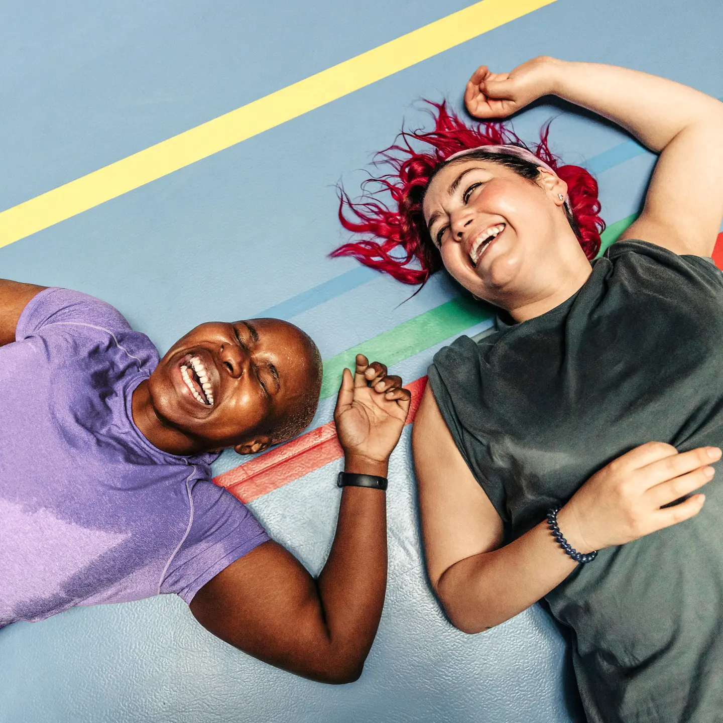 Ein junges Paar liegt lachend und verschwitzt auf dem Boden einer Sporthalle