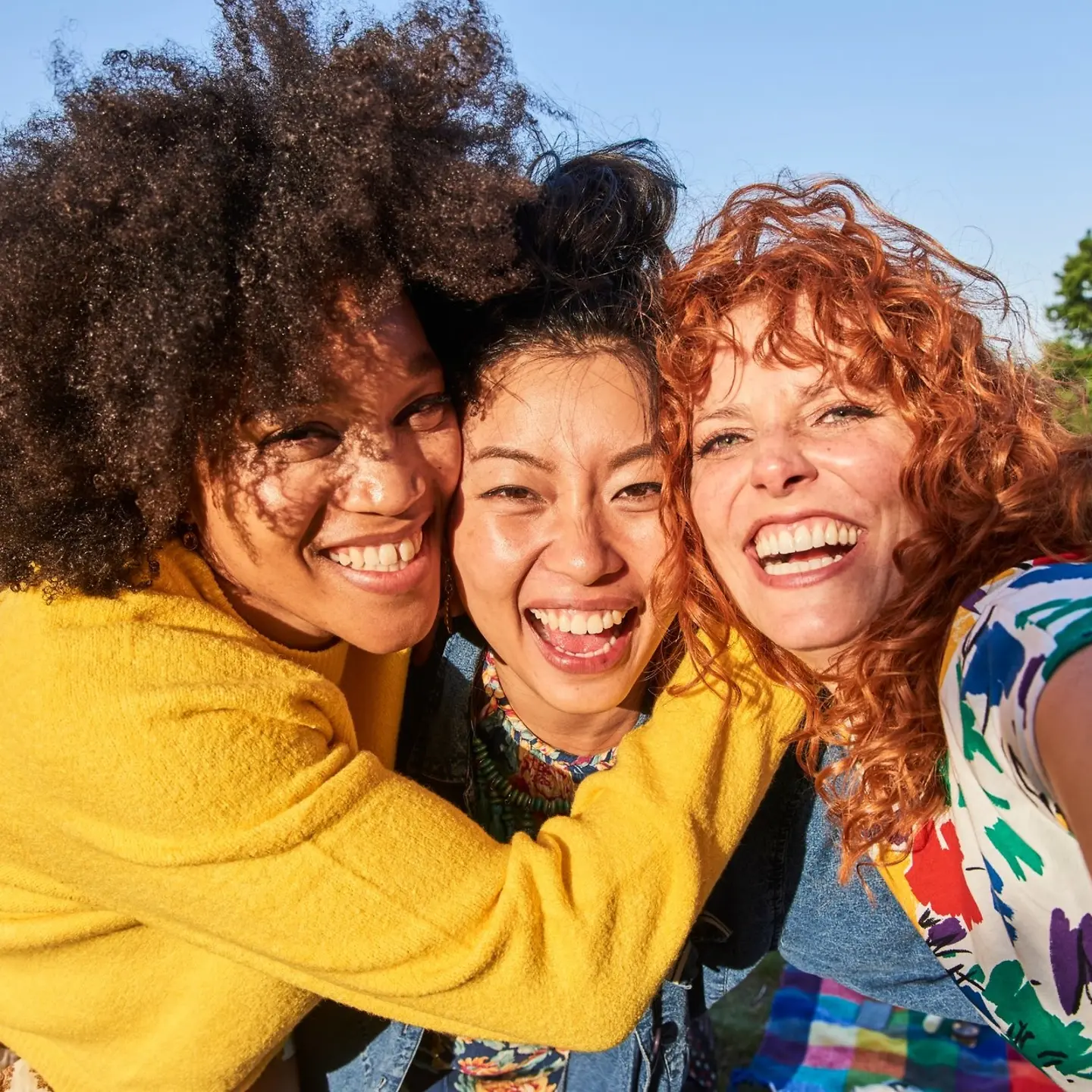 drei junge Frauen lächeln in die Kamera, ihre Gesichter nah beieinander