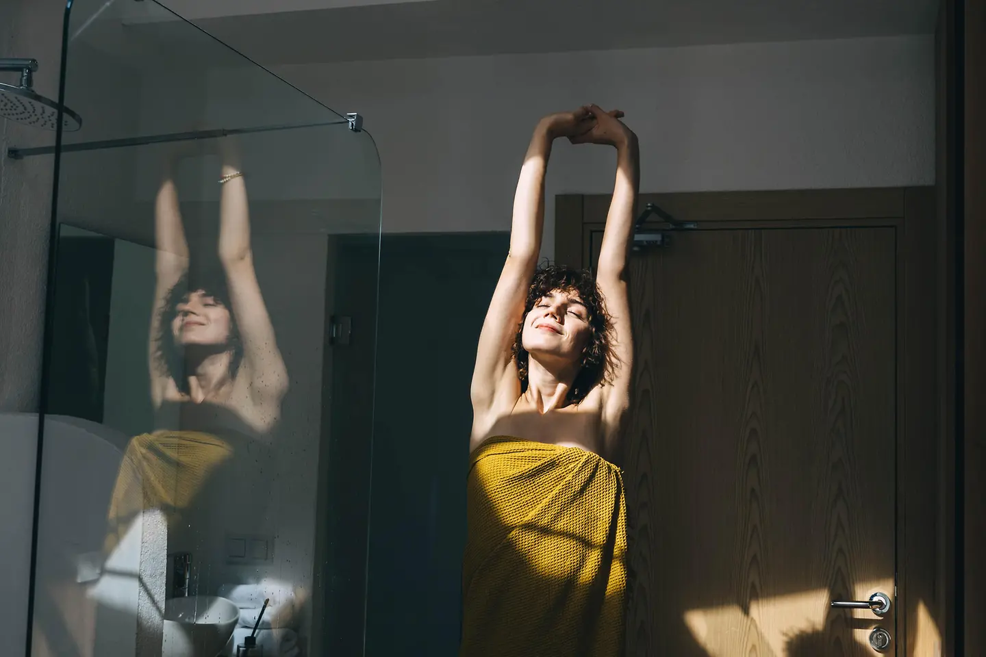 Eine junge Frau mit Handtuch an einem sonnigen Tag im Badezimmer