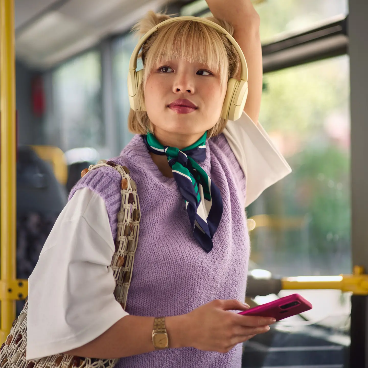 Eine junge Frau mit Kopfhörer und Handy in der Hand steht im Bus und schaut in die Ferne.