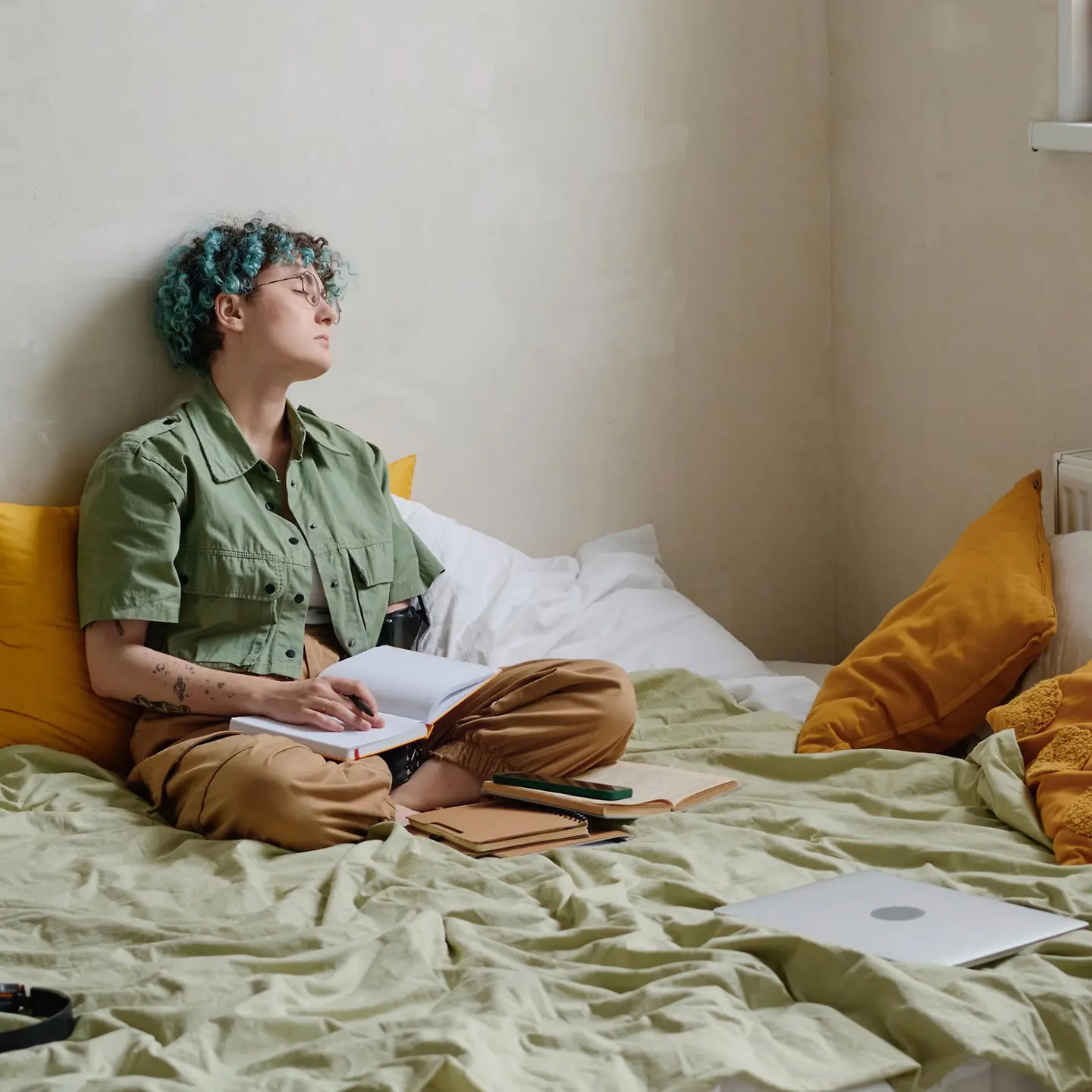 Junge Frau sitzt mit Büchern auf ihrem Bett und döst