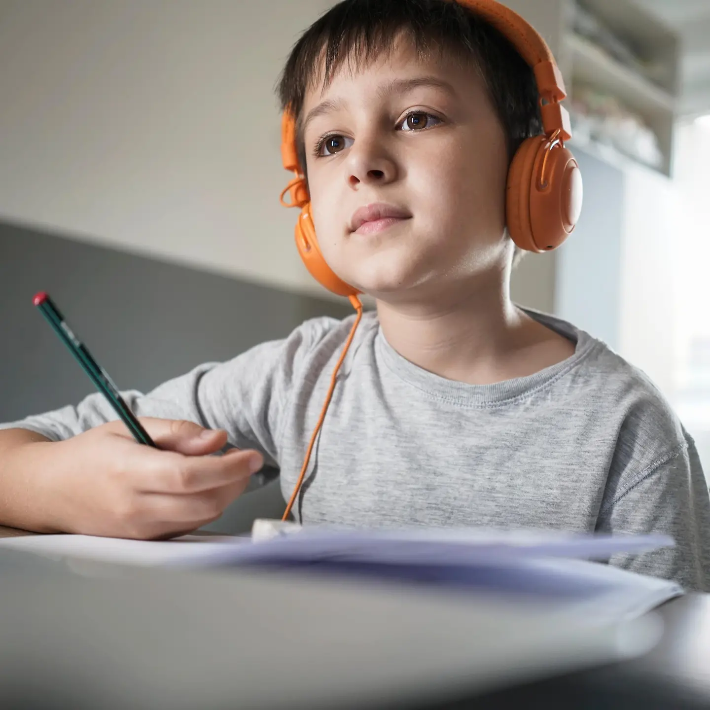 Kleiner Junge mit Kopfhörern sitzt verträumt am Tisch
