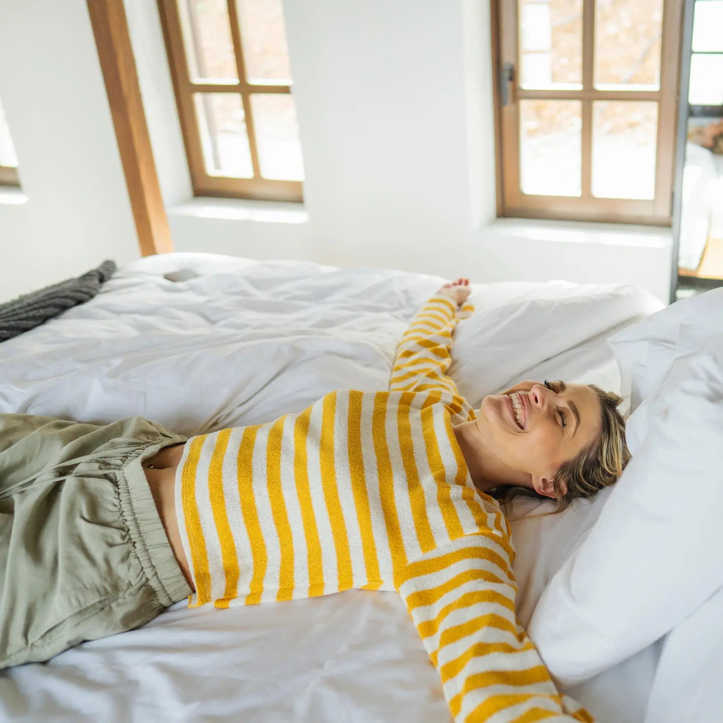 Eine junge Frau liegt auf dem Bett, wacht erholt auf und lacht