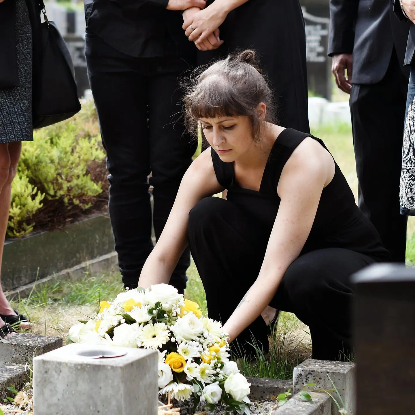 Eine Familie legt bei einer Beerdigung Blumen an ein Grab.