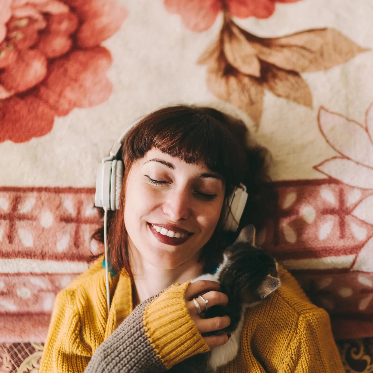 Eine jungen Frau hört Musik mit einem Kopfhörer und schmust mit einer Katze