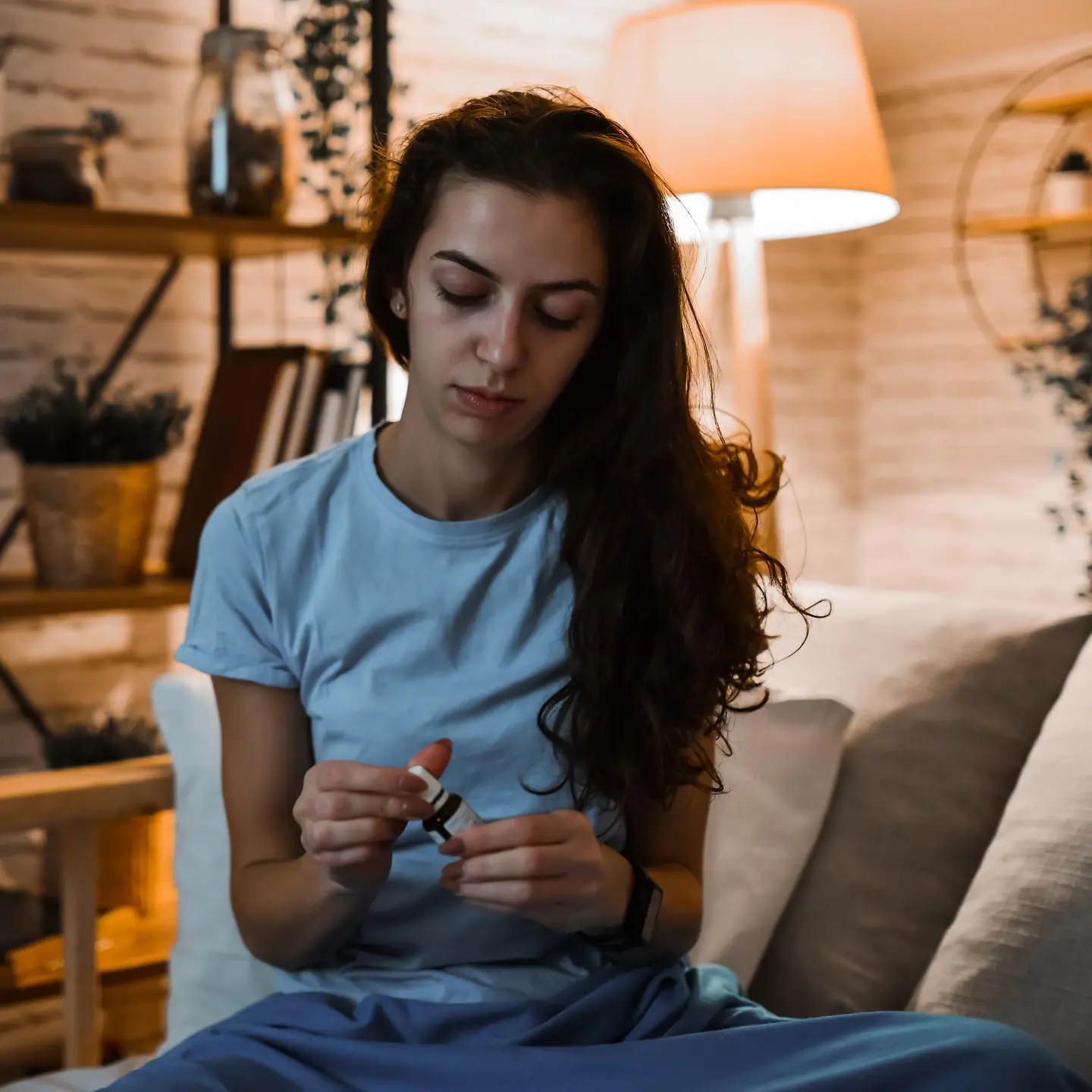 Junge Frau sitzt auf einer Couch und öffnet ein Fläschchen mit einer Arznei